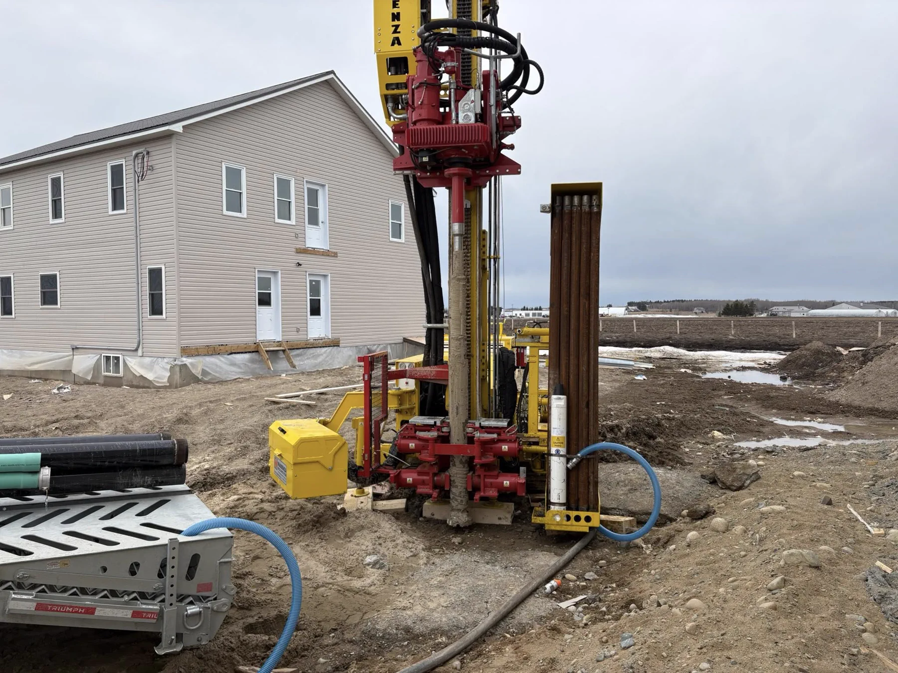 Tracked drill rig positioned vertically beside a construction site.